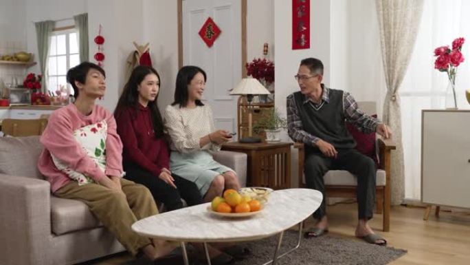 亚洲家庭一起过春节在家看喜剧。母亲使用控制器并推荐带有手势的有趣节目。门上的中文文本翻译: 春天和祝