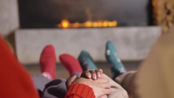 舒适的圣诞节气氛，多元文化的夫妇手牵手，穿着绿色和红色的袜子从一侧到另一侧摇晃双腿