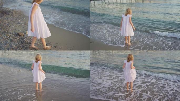 一个穿着白色连衣裙的可爱小女孩赤脚走进冰冷的海水。