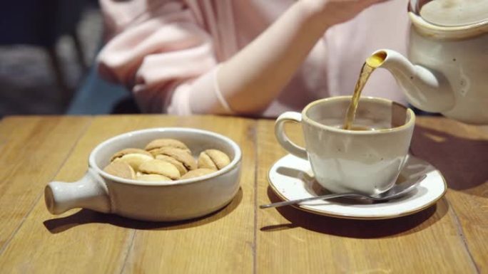 一个女孩将茶壶中的茶倒入杯子中，盘子上放着俄罗斯甜点-核桃形饼干和炼乳