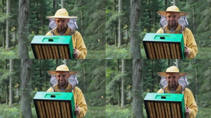 一位从事养蜂工作的年轻经验丰富的微笑男子手中握着蜜蜂的养蜂场，看着他们穿着防护服的工作，脸上戴着蚊帐