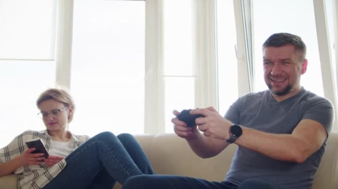 夫妻坐在沙发上玩电子游戏，在恋爱中使用控制器一起玩在线视频游戏很有趣。慢动作