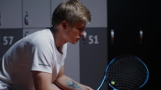 年轻的男性网球运动员赛后休息，坐在更衣室里