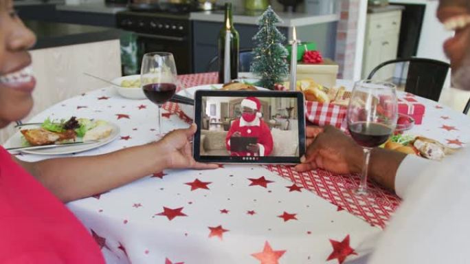 非裔美国人夫妇与葡萄酒使用平板电脑与圣诞老人在屏幕上进行圣诞节视频通话