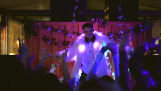 夜总会派对上穿着白色皮大衣的有趣男dj与夜总会的人跳舞。