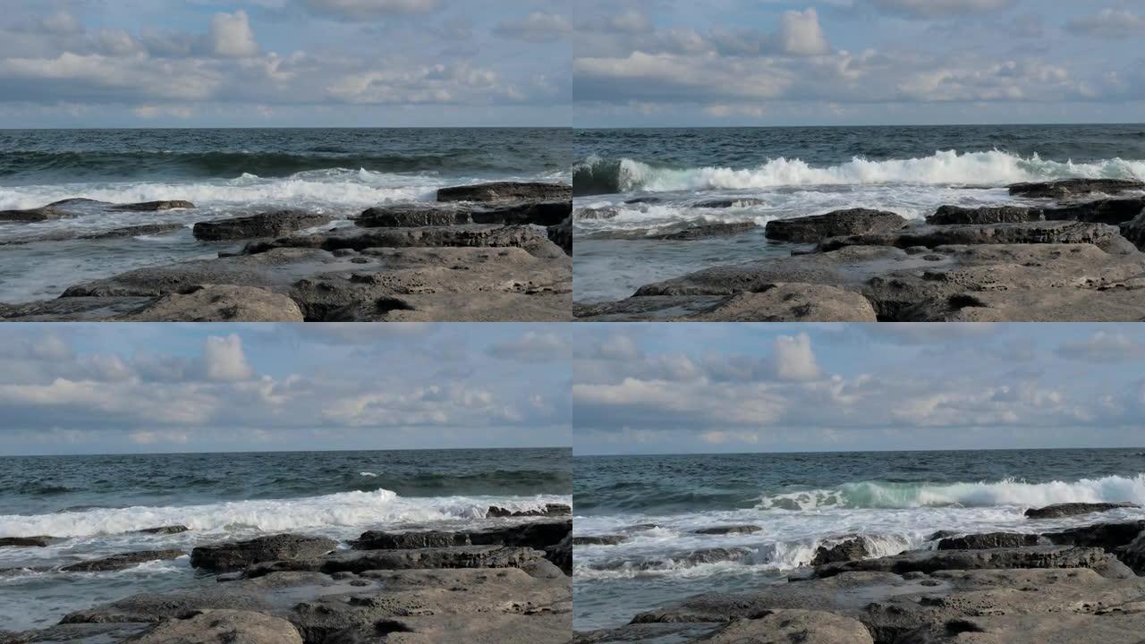 海浪溅落在蓝色海洋背景的岩石海岸上。波涛汹涌的岩石海岸线在暴风雨中席卷而来。海浪用泡沫在石头上破裂。