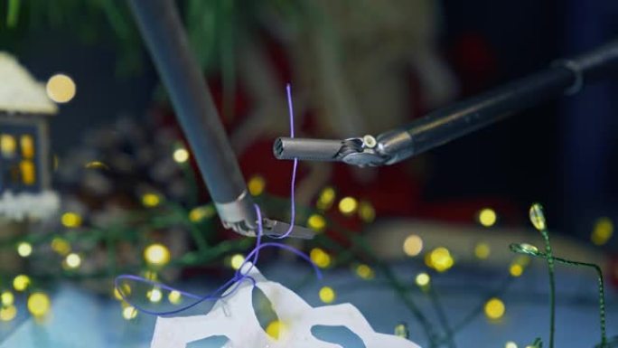 达芬奇系统的小镊子在线上打结。通过达芬奇外科手术系统的机械臂将线紧固在雪花纸上。特写。
