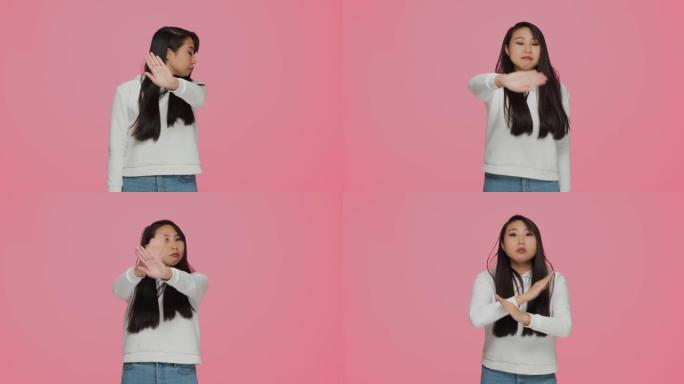 严肃的年轻亚洲女孩确实停止手势，否认不好的提议，说不，拒绝粉红色工作室背景上的建议