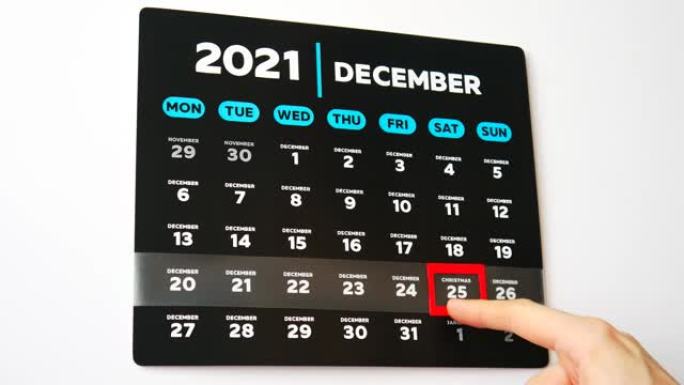 挂历2021的黑色美丽12月页面的特写和一只男性手将红色光标移动到圣诞节日期