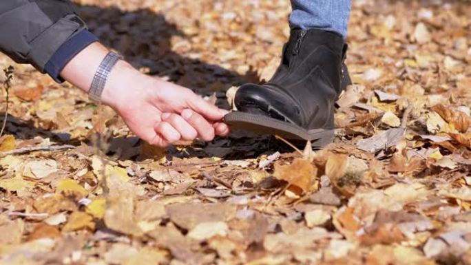 女性展示了一只撕裂的鞋子，站在秋天树林中郁郁葱葱的落叶上