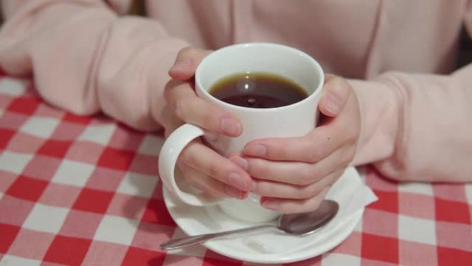 咖啡馆的一个女孩访客用手拿着一杯热茶，上面装有甜叶菊或蔗糖