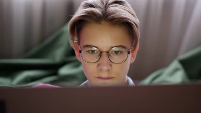 戴着眼镜的十几岁男孩看着笔记本电脑屏幕