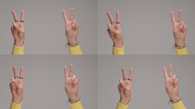 男人的手在空中握着手指，在工作室的灰色背景前做出和平手势