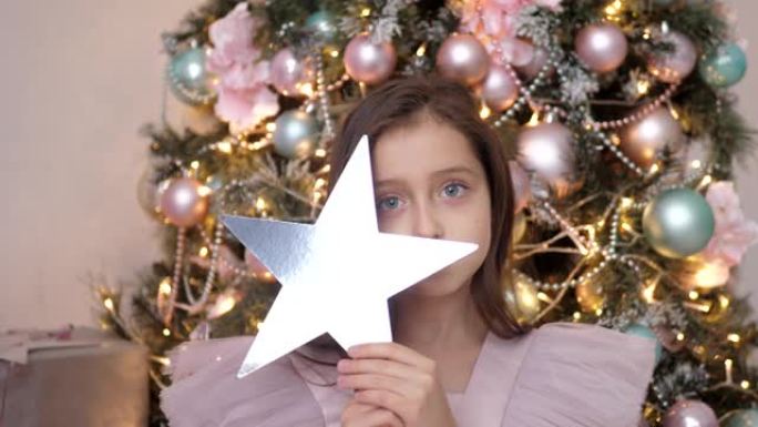 美丽的高加索女孩穿着粉红色连衣裙在圣诞树上评判，并拥有一颗星星