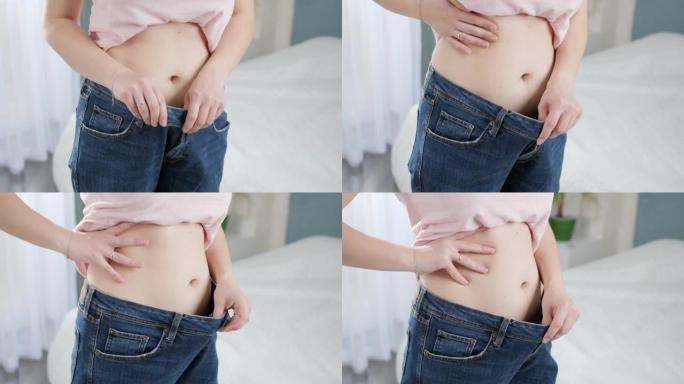 年轻苗条的女人，平坦的腹部，穿着大牛仔裤，展现出完美的身材。节食、减肥和健康的生活方式的概念。