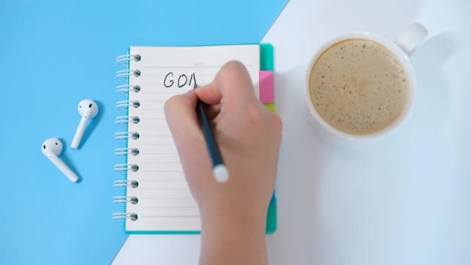 女手在白色和蓝色背景的笔记本上写下目标。