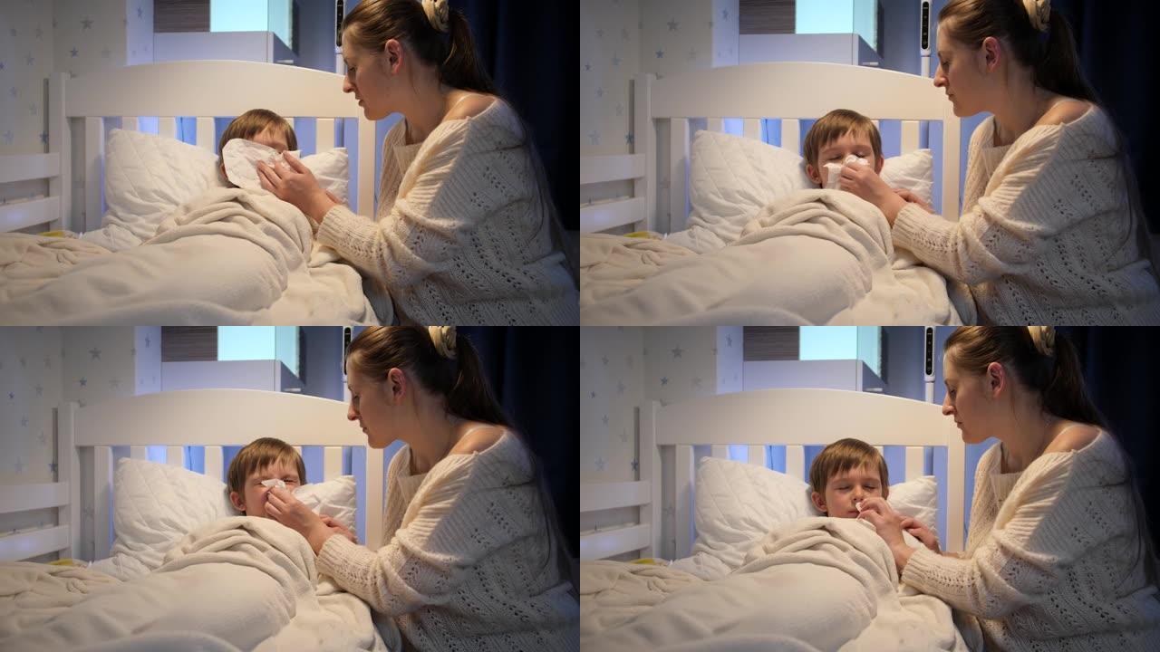 年轻的有爱心的母亲坐在生病的儿子旁边，用纸巾吹鼻子。儿童疾病、疾病和父母护理的概念