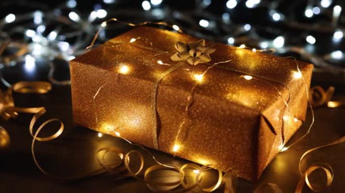 闪烁背景上的灯串包裹着金色圣诞礼物