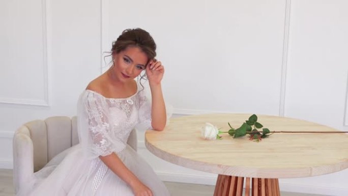 穿着白色连衣裙的新娘坐在桌子旁为摄影师摆姿势
