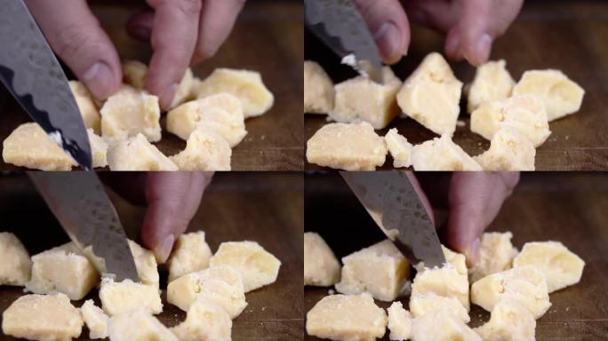 硬奶酪块。一个人在砧板上切奶酪。硬奶酪品种。帕尔马干酪。