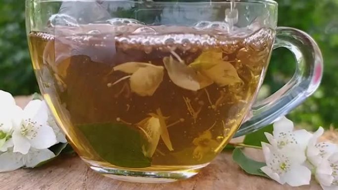 一杯绿茶配花茉莉花。木质背景上的茉莉花茶和茉莉花。茉莉花和叶。慢动作将茶倒入杯子中，然后用茶匙搅拌近
