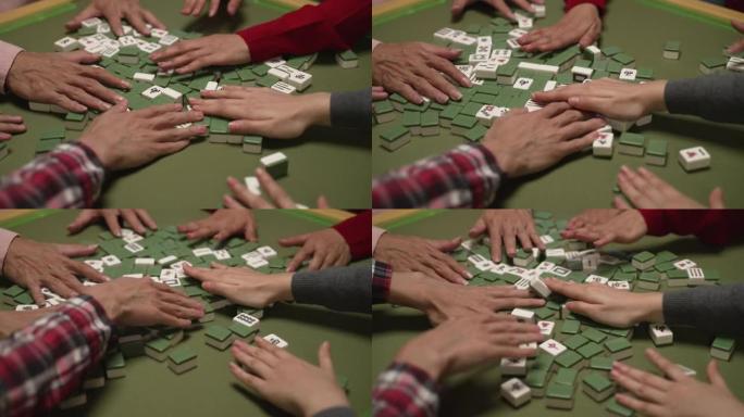 特写镜头，双手在麻将桌上拖着绿色的白色瓷砖。中国春节概念的传统室内娱乐