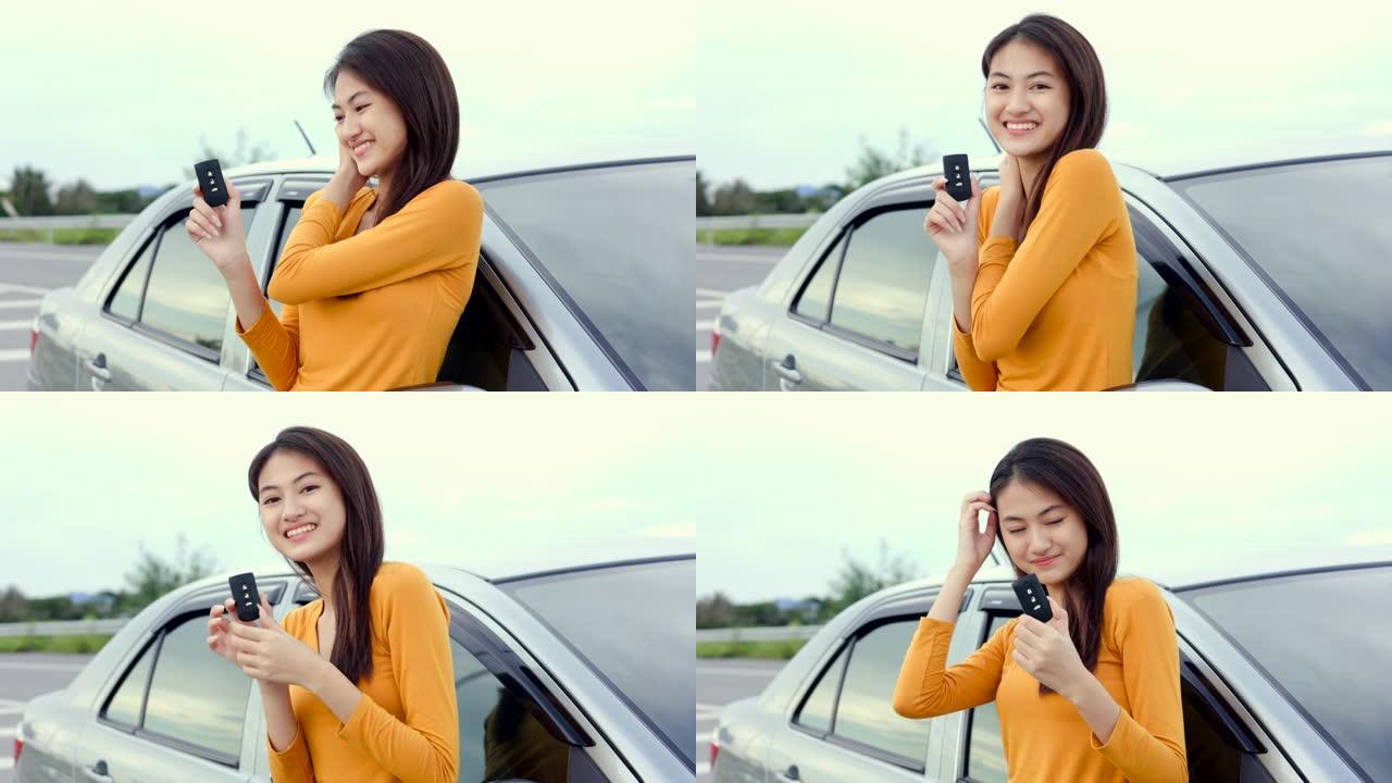 年轻漂亮的亚洲女性购买新车。她站在路边的汽车附近。手展示车钥匙。灿烂的日子里，微笑的女性驾驶车辆在路