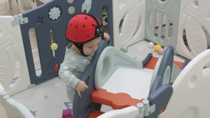 可爱的婴儿安全帽幼儿玩滑梯游戏。婴儿和幼儿安全活动中心游戏场，使儿童远离伤害。