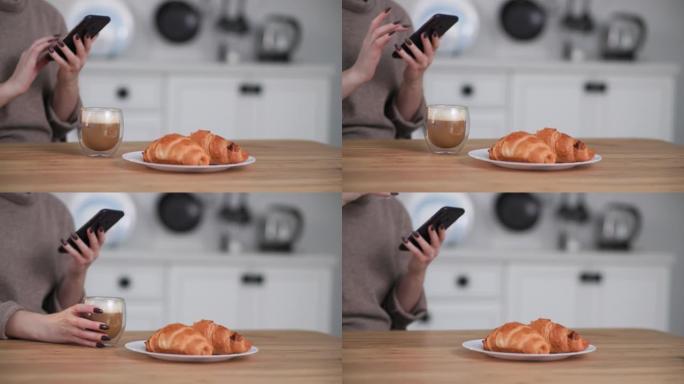 年轻女子坐在家里放松时，用手机在社交媒体上给朋友拍了卡布奇诺和羊角面包的早餐