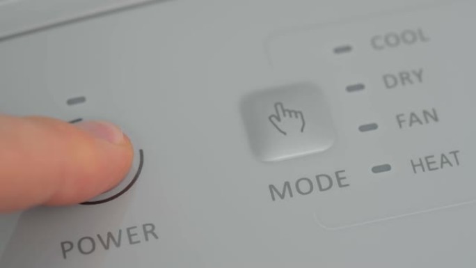 该人用手指在移动空调上按下启动按钮，以在冬天为房间预热。特写。