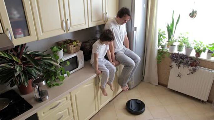 父子俩抬起双腿，让机器人吸尘器清理厨房的地板