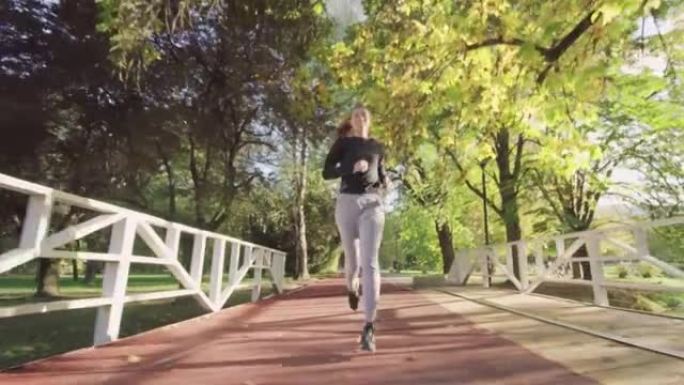 健身女孩在公园木桥上的全天候合成跑道上奔跑。全身射击