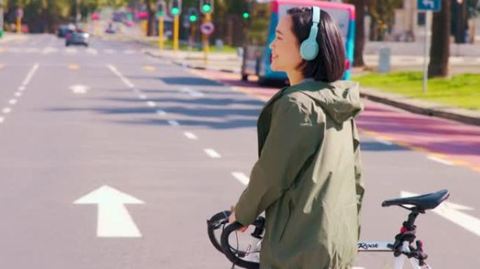 4k视频片段，一个漂亮的年轻女孩穿过街道，推着自行车穿过街道，戴着耳机