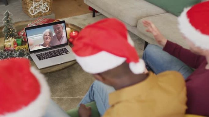 拥有圣诞老人帽子的多元化家庭使用笔记本电脑进行圣诞节视频通话，屏幕上有幸福的夫妇
