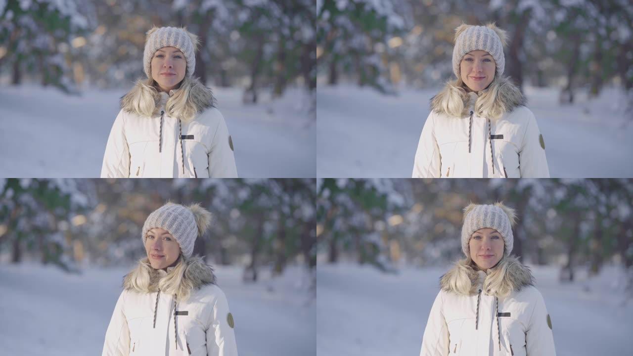 一个穿着暖和冬装的可爱的女孩看着相机微笑的肖像。年轻女子在白雪皑皑的森林模糊背景下在户外摆姿势。特写