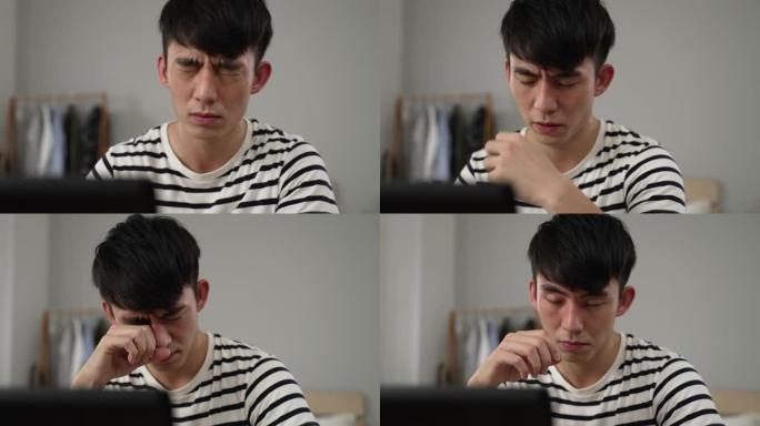 一个过度劳累的韩国年轻人的特写镜头突然视力模糊，正在在家计算机上工作时揉眼睛。
