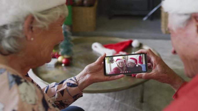 微笑的高加索高级夫妇使用智能手机与屏幕上的夫妇进行圣诞节视频通话