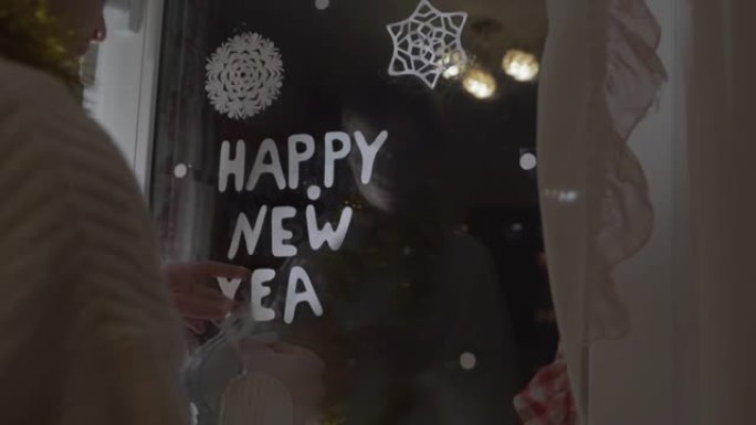 十几岁的女孩用纸字母装饰窗户玻璃新年快乐
