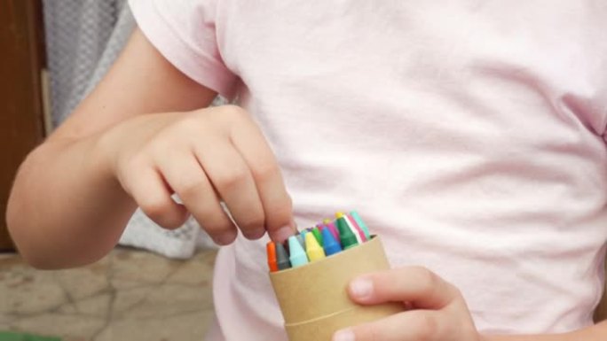 匿名的孩子，小学年龄的女孩手里拿着一盒五颜六色的蜡笔，选择蜡笔，细节，特写。儿童和艺术用品、色彩、创