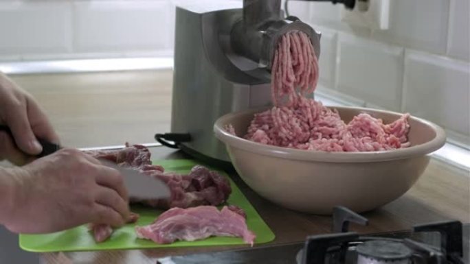 通过电动研磨机从新鲜猪肉中制备自制碎肉。男人的手在厨房里用刀切生肉。在家做饭，健康饮食和生活方式。选