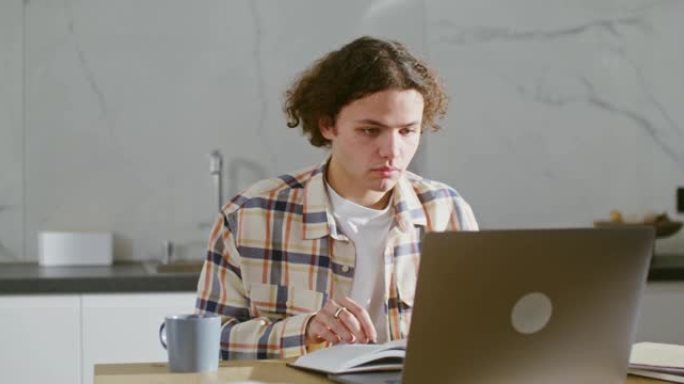 一个年轻人使用笔记本电脑，坐在桌子旁，摆放着许多书籍和笔记本