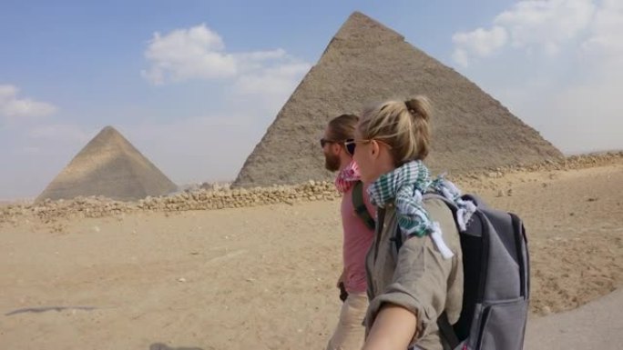 年轻夫妇使用自拍杆在埃及旅行，参观开罗的大金字塔。
