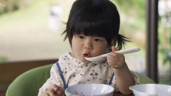 特写镜头，一个无辜的女蹒跚学步的孩子在早餐时间用叉子从碗里吃美味的果酱。