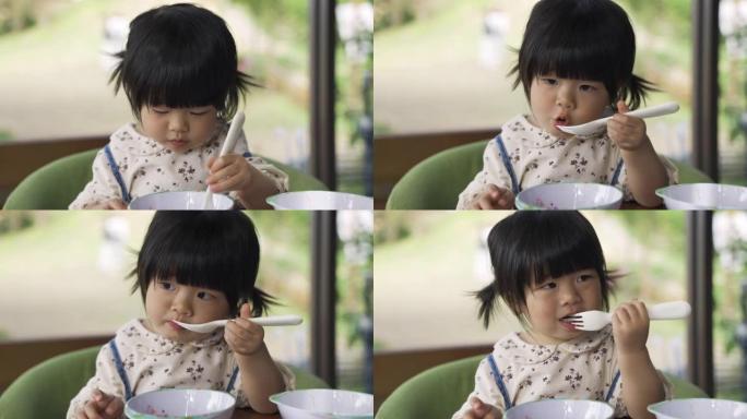 特写镜头，一个无辜的女蹒跚学步的孩子在早餐时间用叉子从碗里吃美味的果酱。