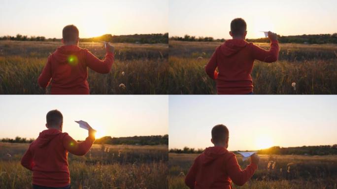 小男孩用纸飞机在草地上慢跑。无忧无虑的小孩带着玩具飞机在日落背景下的草地上奔跑。可爱的孩子在大自然中