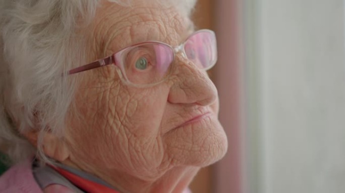 有深深的皱纹的老女人。白发的祖母看着窗外