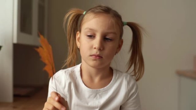 沉思小女孩的特写肖像手握在一起，若有所思地旋转干燥的秋叶枫树，思考要制作什么贴花或图片。