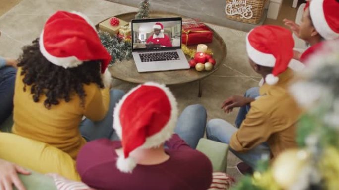 拥有圣诞老人帽子的多元化家庭使用笔记本电脑进行圣诞节视频通话，屏幕上有快乐的圣诞老人