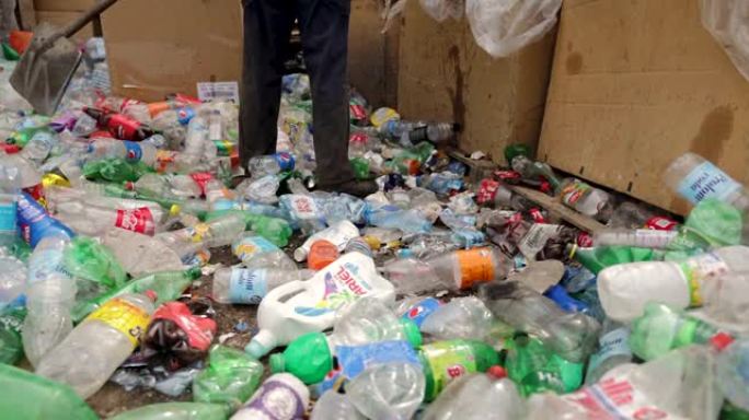 在回收工厂，无法辨认的工人用chovel整理塑料瓶