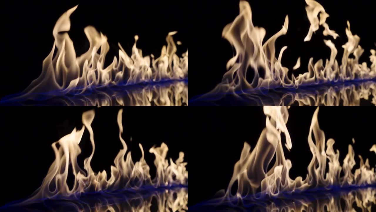 在黑色反射背景上，火以慢动作点燃并燃烧。易燃燃料或汽油的污渍在黑暗中燃烧释放能量和蓝光。火光